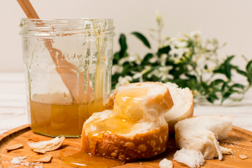 Honig in einem Glas, daneben Brotscheiben mit Honig
